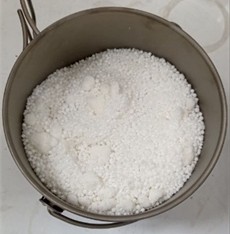 Loading of urea and potash (600 g) into the titanium crucible. Photo by the authors in the  laboratory of the Almalyk Branch  of NUST MISIS 2026