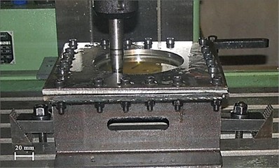 Single point incremental forming of the St14-AA3105 laminated sheet: a) schematic of the process, showing the clamped bi-layer blank with the AA3105 layer facing the tool, the hemispherical tool, the vertical step size ∆z, the wall angle α, and the helical contour tool path; b) experimental setup on the three-axis CNC milling machine